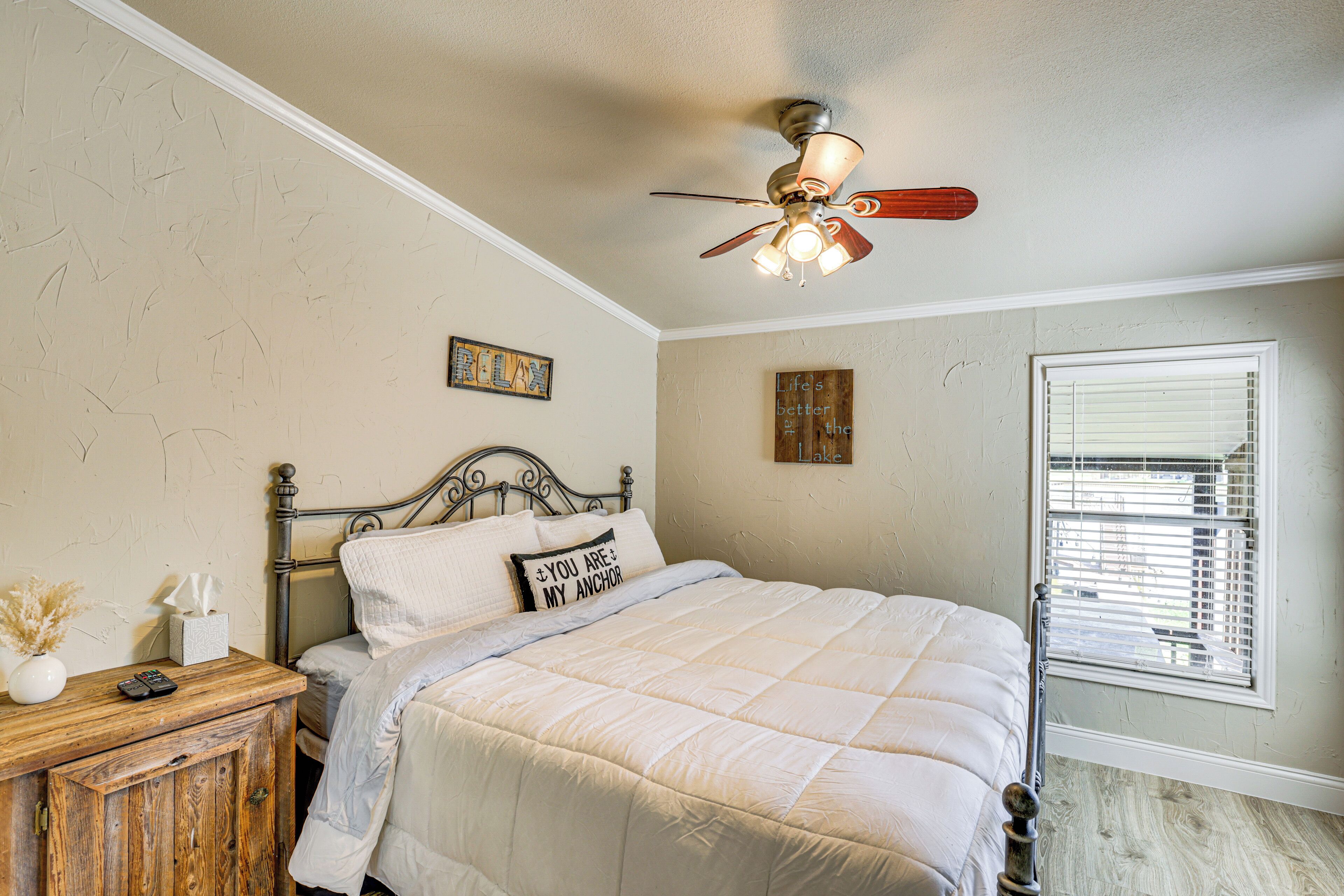 A bedroom with a bed, a wooden nightstand, a ceiling fan, and a window with blinds.