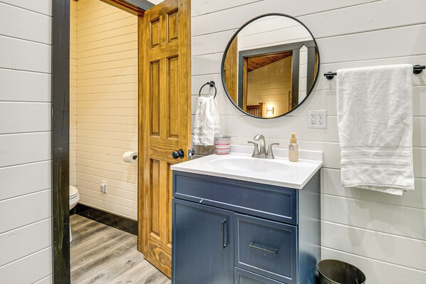 A bathroom with a wooden door, a round mirror, a white sink, and a blue cabinet.