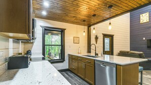 A modern kitchen with wooden cabinets, a stainless steel dishwasher, and a large window. - Red River Gorge Barndominium: Dog Friendly! (Beattyville)