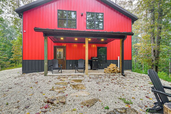 A red cabin with a covered patio area, stone steps, and outdoor seating.