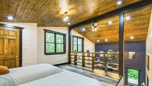 A bedroom with two beds, wooden ceiling, large windows, and a balcony with plants. - Red River Gorge Barndominium: Dog Friendly! (Beattyville)