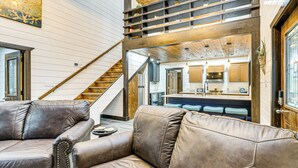 A spacious living area with leather sofas, a wooden staircase, and a modern kitchen in the background. - Red River Gorge Barndominium: Dog Friendly! (Beattyville)