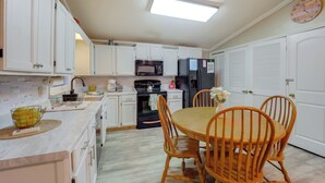 A modern kitchen with white cabinets, a microwave, a refrigerator, and a dining area with wooden chairs and a table. - Community Perks! Mountain Home w/ Deck in Newland (Newland)