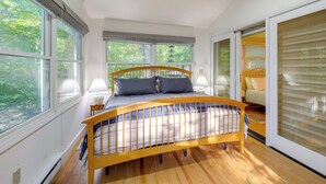 A bedroom with a wooden bed, large windows, and a view of the outdoors. - Community Perks! Mountain Home w/ Deck in Newland (Newland)