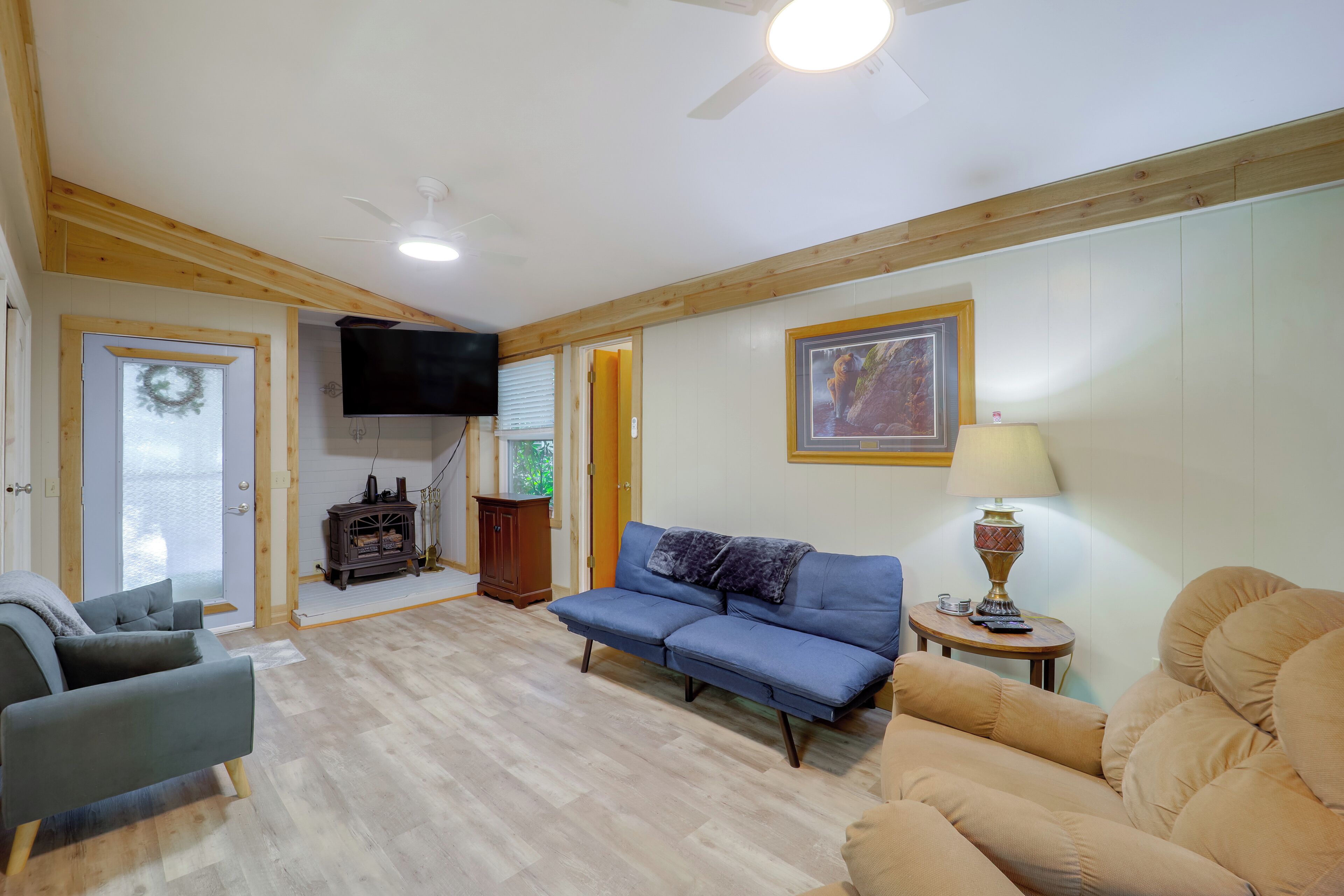 A living room with a blue sofa, a beige sofa, a wooden cabinet, a television, and a ceiling fan.