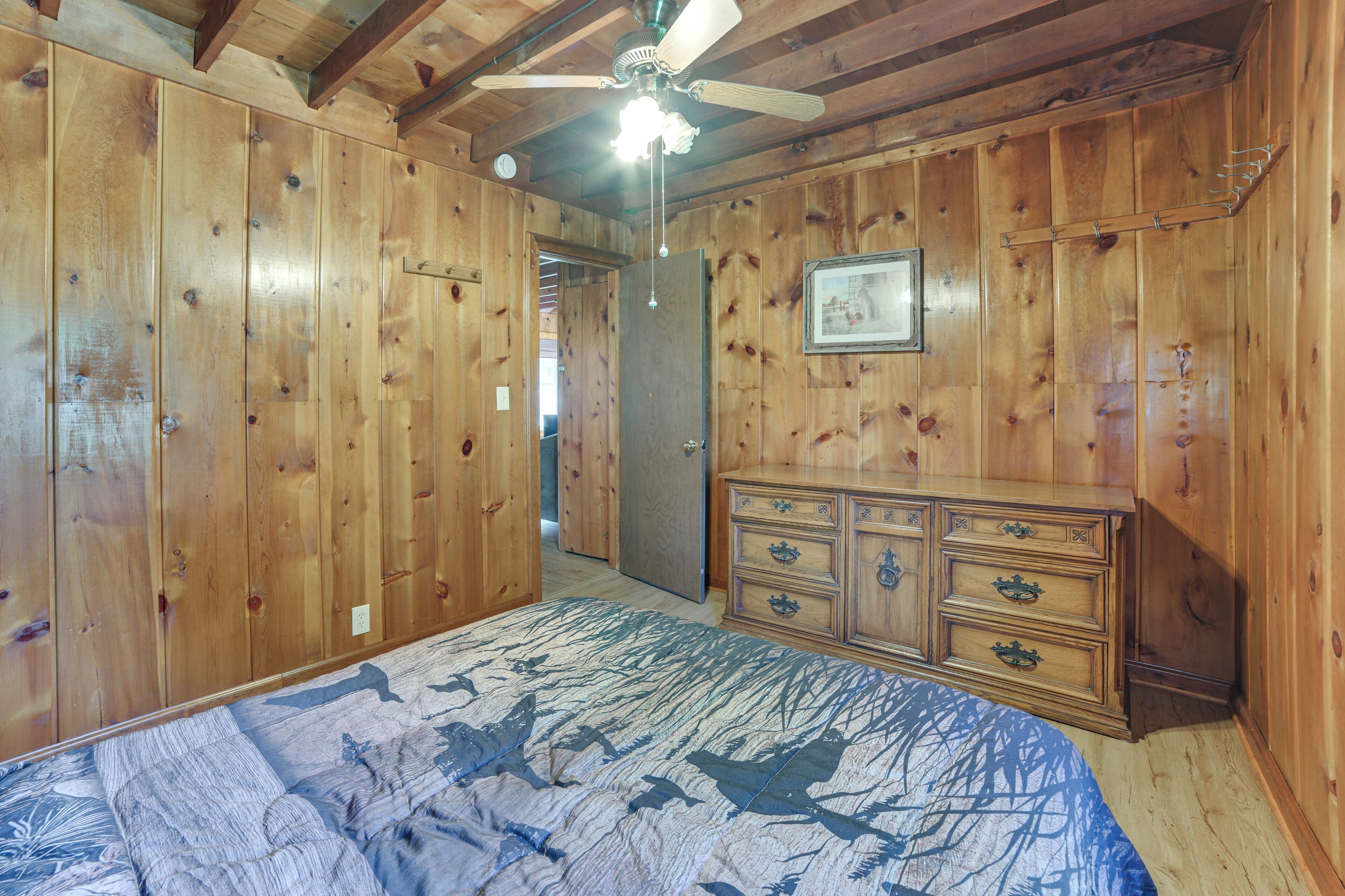 A room with wooden paneling, a ceiling fan, a bed with a patterned bedspread, and a dresser with drawers.