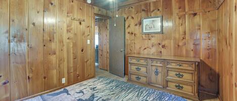 Une pièce avec des lambris en bois, un ventilateur de plafond, un lit recouvert d’une couvre-lit à motifs et une commode avec des tiroirs.