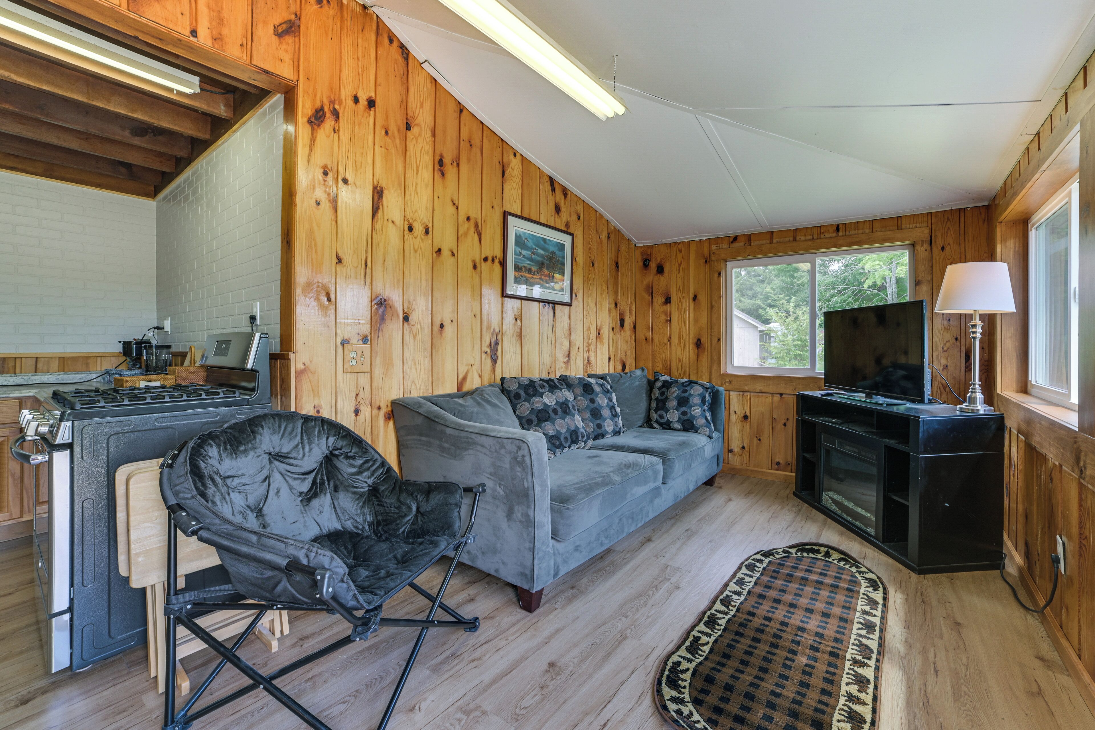 Interior acogedor de una cabaña con kitchenette, sofá gris y televisor.