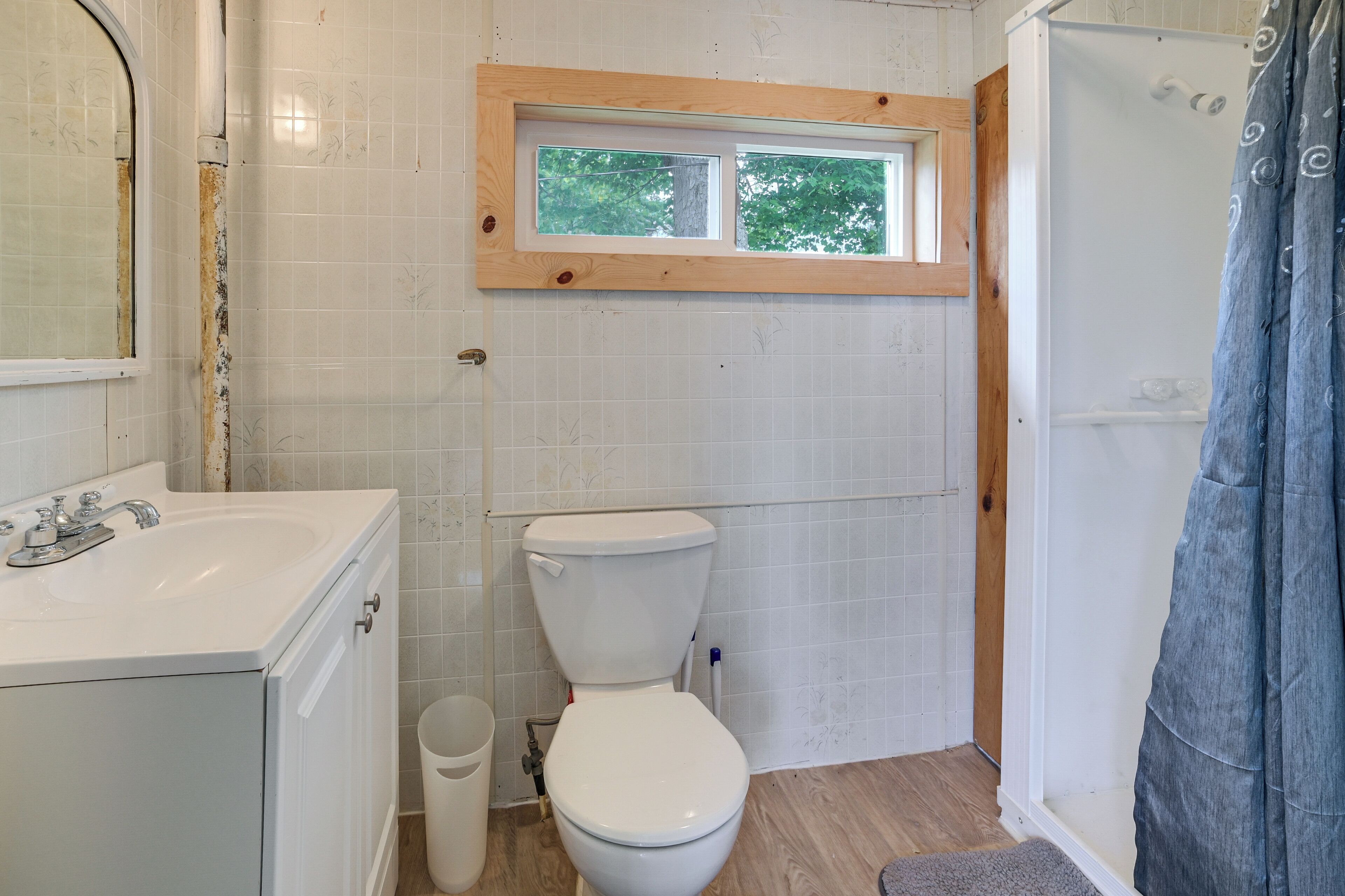 Un baño con inodoro blanco, lavamanos y ventana sobre el inodoro.