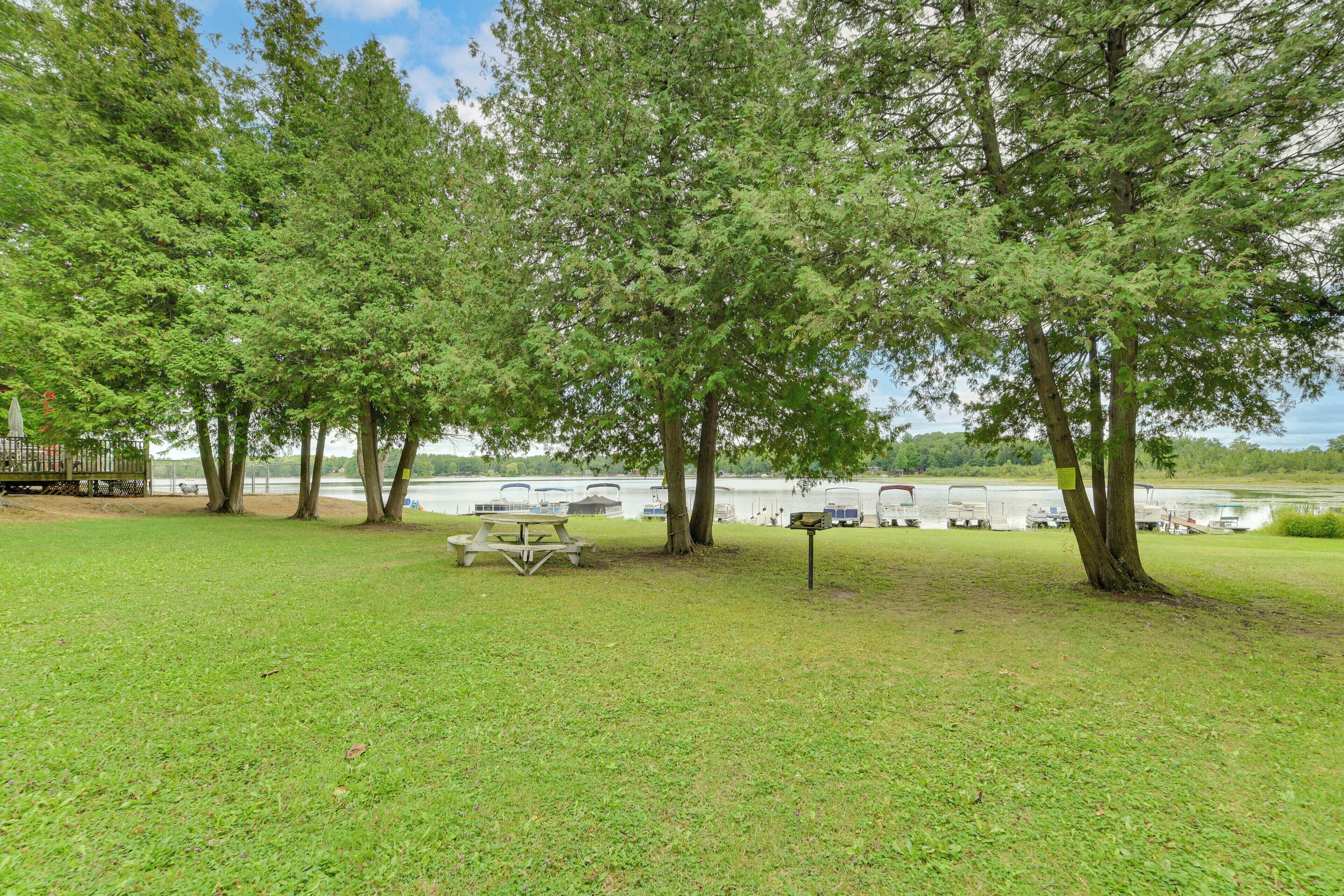 A grassy area with picnic tables and trees, a lake in the background, and RVs parked along the shore.