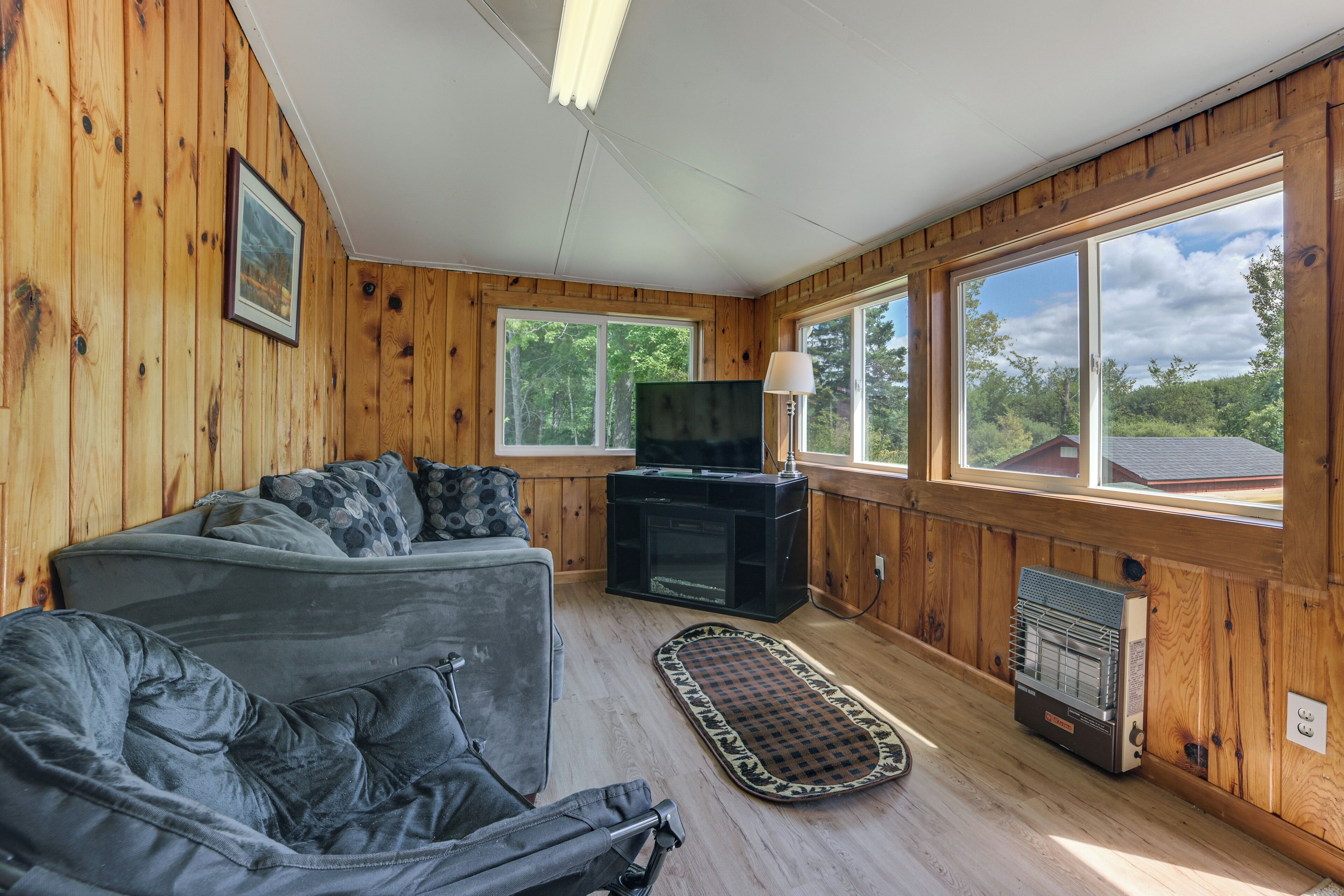 A cozy cabin interior with a gray sofa, a television, and a fireplace.