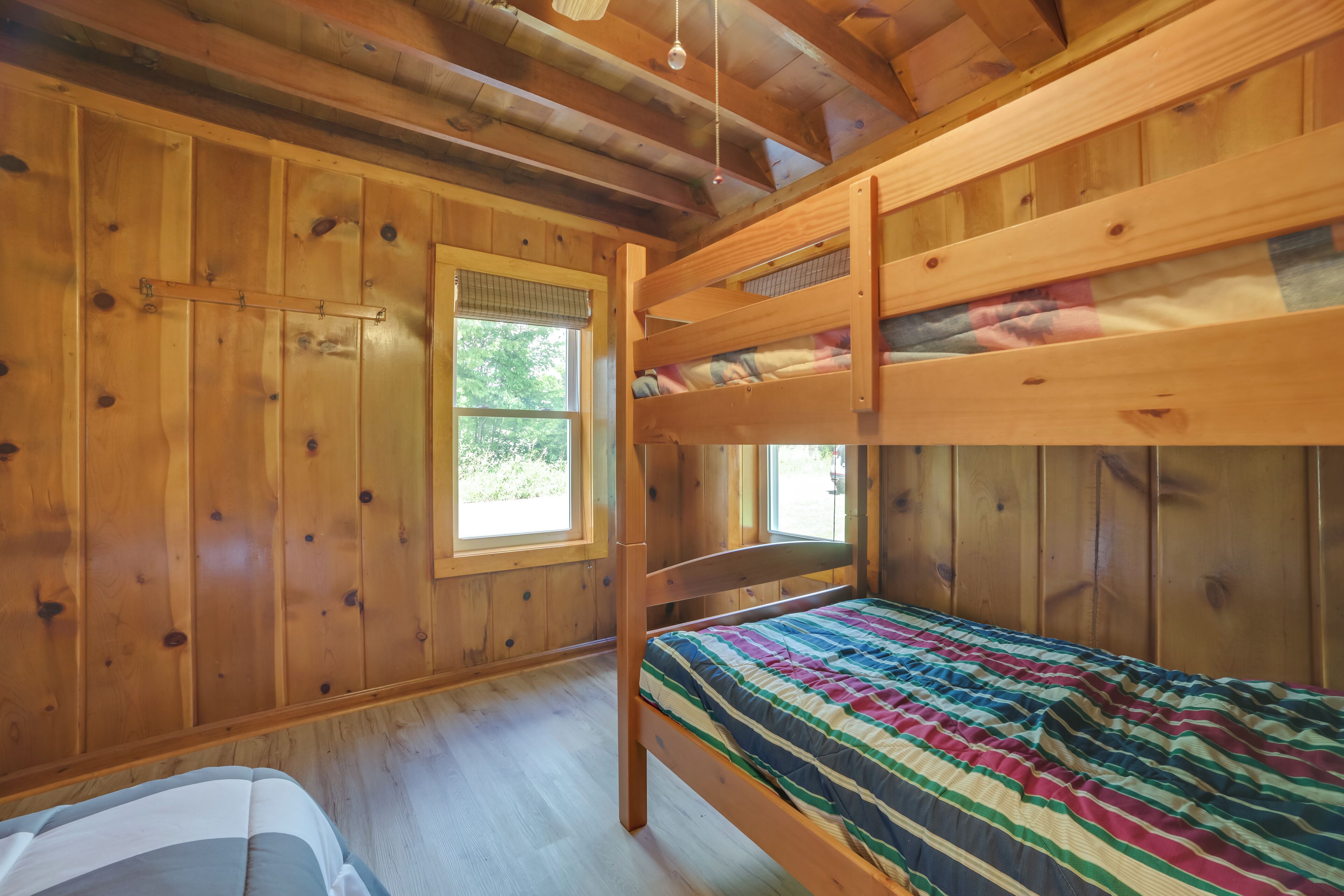 Ein Zimmer in einer Holzhütte mit Etagenbetten, einem Fenster und einem Bett mit einer gestreiften Decke.