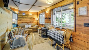 Un interior de cabaña acogedor, con paredes de madera, una chimenea, una mesa de comedor con sillas, un sofá y una computadora portátil sobre una mesa.