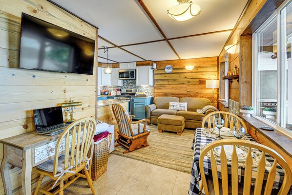 A cozy cabin interior with a dining area, kitchen, and a TV mounted on the wall. - Hood Canal Views: Remote Cabin in Quilcene! (Quilcene)