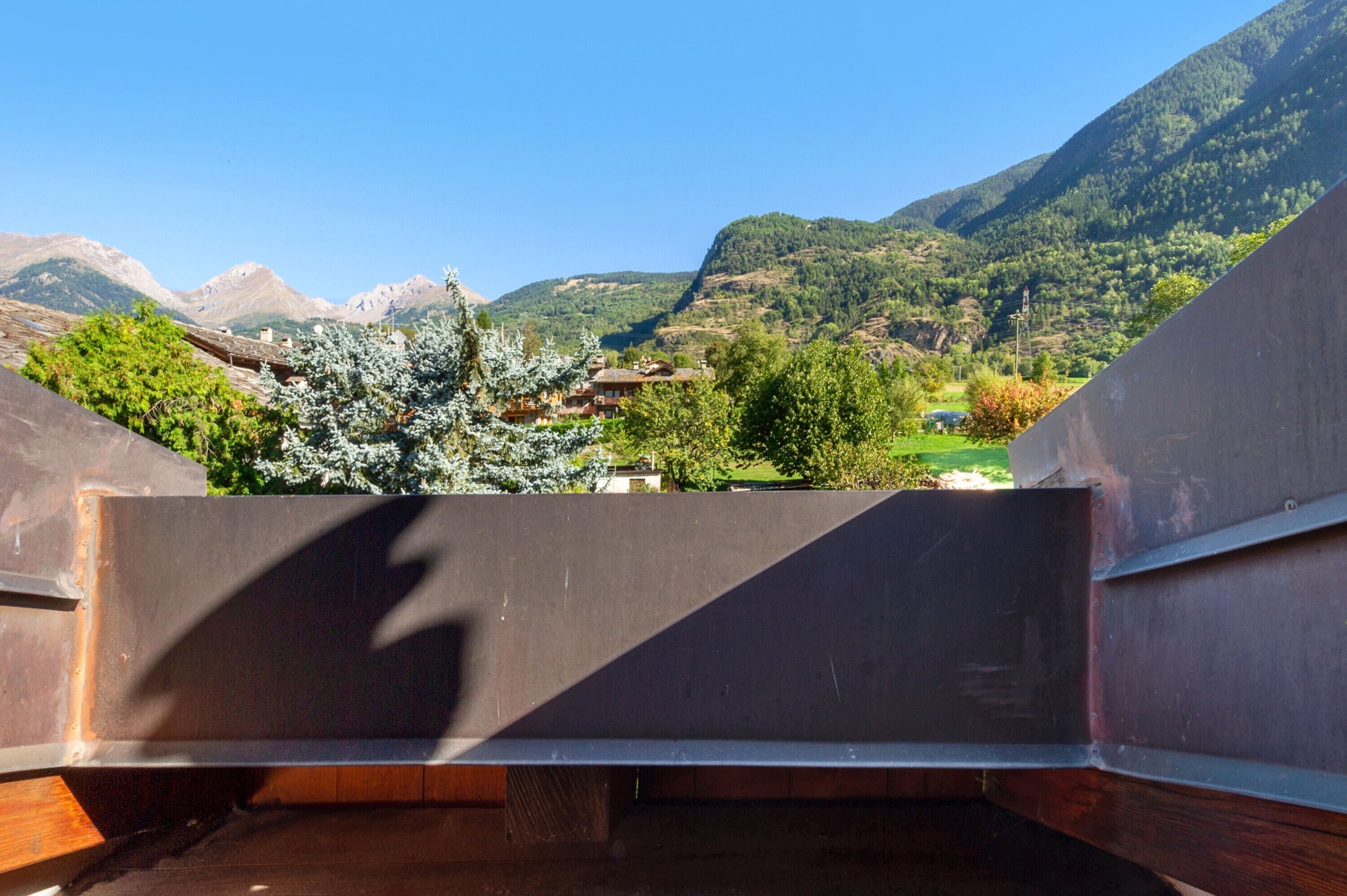 Paesaggio montuoso con cielo sereno, un edificio con tetto spiovente e un albero con chioma bianca.