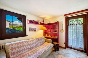 A cozy room with a patterned sofa, a red bookshelf, a small stool, and a window with a view of mountains.
