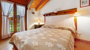 Ein Schlafzimmer mit Holzboden, einem Bett mit floralem Überwurf, zwei Nachttischlampen und einem Fenster mit Vorhängen.