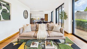 A modern living room with a sofa, coffee table, and a view of the kitchen and outside. - Stunning Camden Town Balcony Apartment (Greater London)