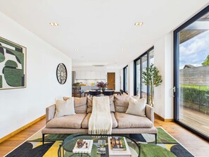 A modern living room with a sofa, coffee table, and a view of the kitchen and outside.