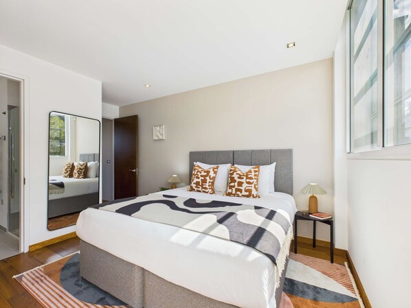 A modern bedroom with a large bed, a bedside table, a nightstand, and a mirror.