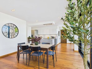 A modern dining area with a round table and chairs, a decorative vase, and a large wall clock. - Stunning Camden Town Balcony Apartment (Greater London)
