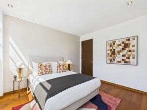 A modern bedroom with a large bed, a nightstand, a lamp, a door, and a wall art piece. - Stunning Camden Town Balcony Apartment (Greater London)
