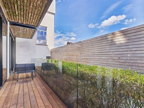 A modern outdoor deck with a wooden floor, a glass balustrade, and a wooden wall.