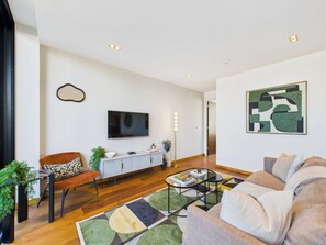 Ein modernes Wohnzimmer mit einer Couch, einem Sessel, einem Couchtisch und einem an der Wand befestigten Flachbildfernseher.