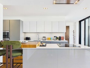 A modern kitchen with white cabinets, a central island, and a dining area with a green chair.
