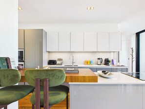 A modern kitchen with white cabinets, a wooden countertop, and a dining area with green upholstered chairs. - Stunning Camden Town Balcony Apartment (Greater London)