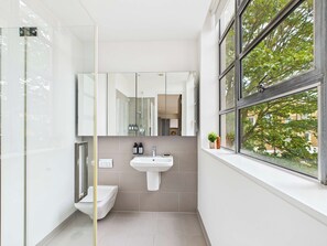 A modern bathroom with a glass shower enclosure, a white sink, and a window with a view of trees.