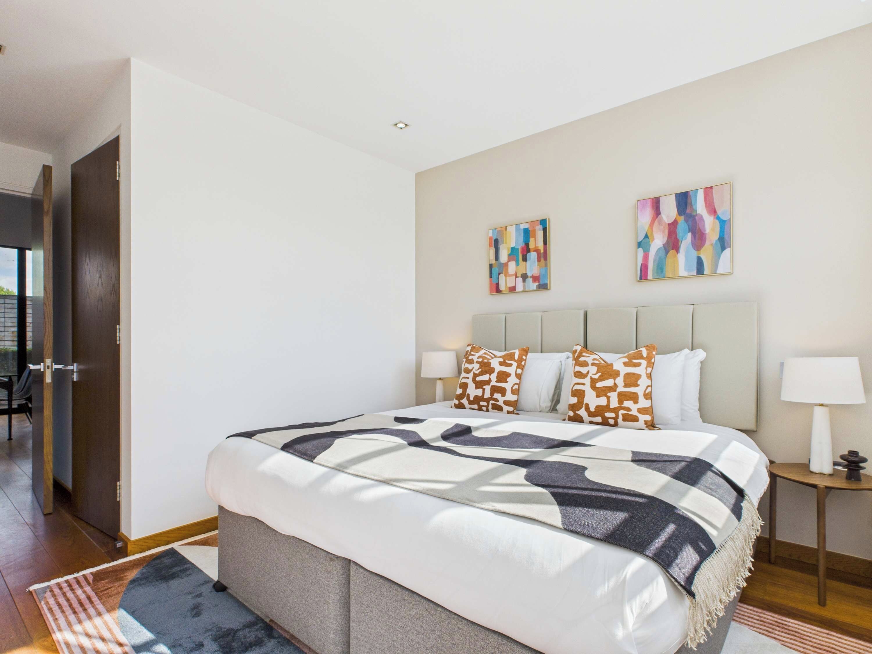 A modern bedroom with a large bed, two side tables, and abstract wall art.