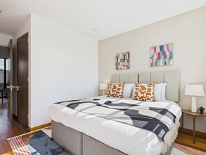 A modern bedroom with a large bed, two side tables, and abstract wall art.