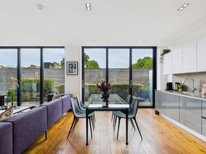 Una cocina moderna con ventanas amplias, un comedor con mesa de vidrio y un sofá.