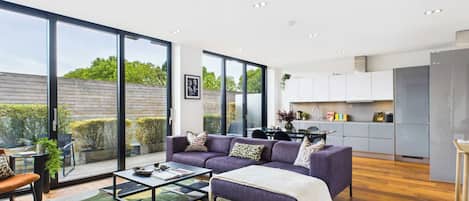 Una sala de estar moderna con un conjunto de sofás, una mesa de centro y vistas del jardín a través de amplios ventanales correderas.