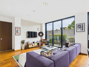 A modern living room with a large TV, a sofa, a coffee table, and a view of the outside.