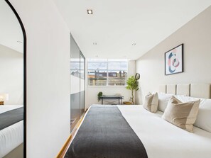A modern hotel room with a large bed, a desk, and a view of the city through the window.