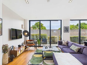 Un salon moderne doté d’un grand téléviseur, de sièges confortables, d’une table basse et offrant une vue sur le jardin à travers de grandes portes coulissantes.