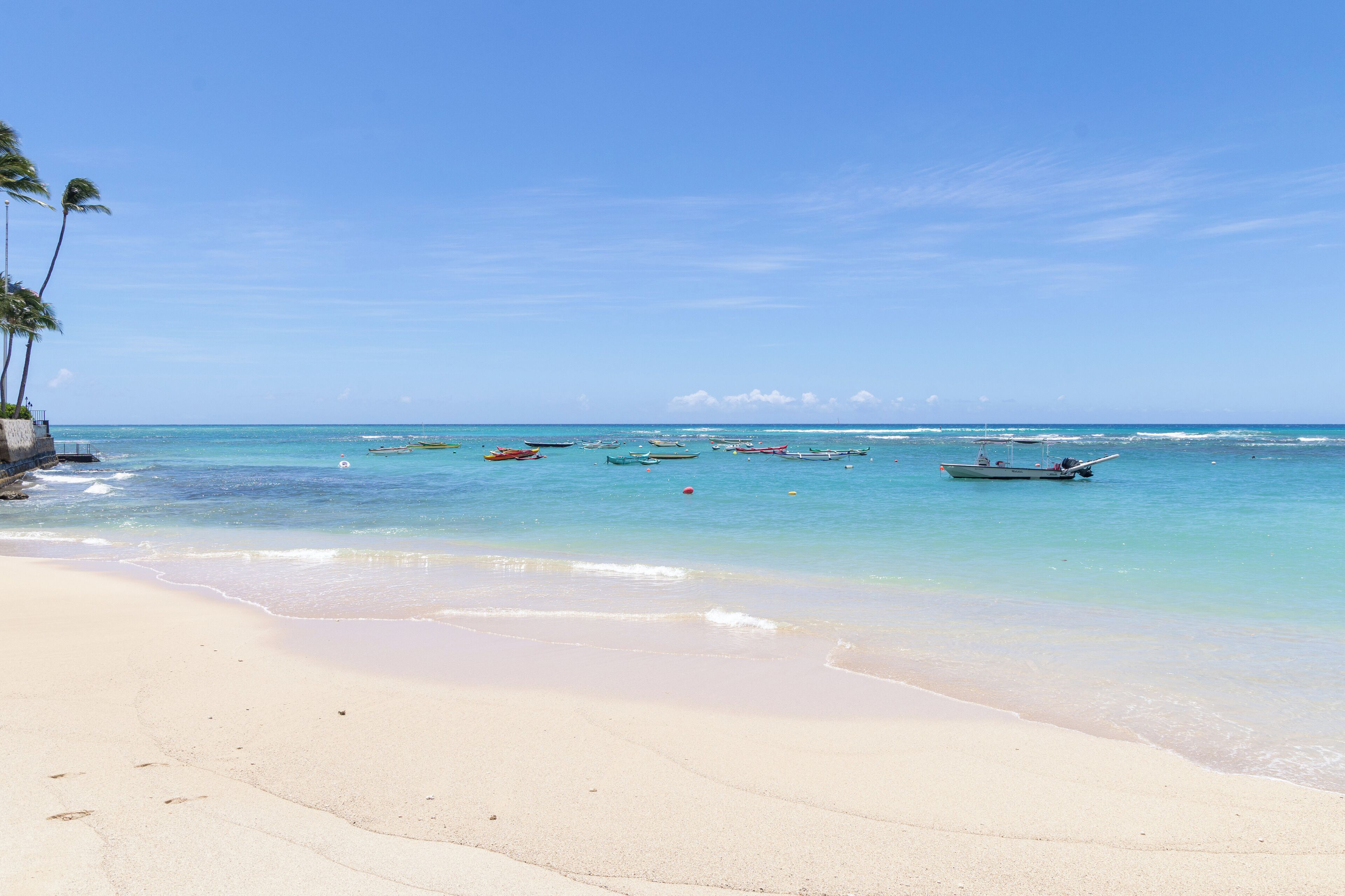 A beach with clear turquoise water, several boats anchored near the shore, and a sandy beach with palm trees.