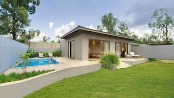 A modern house with a swimming pool, a patio with chairs, and a well-maintained lawn.