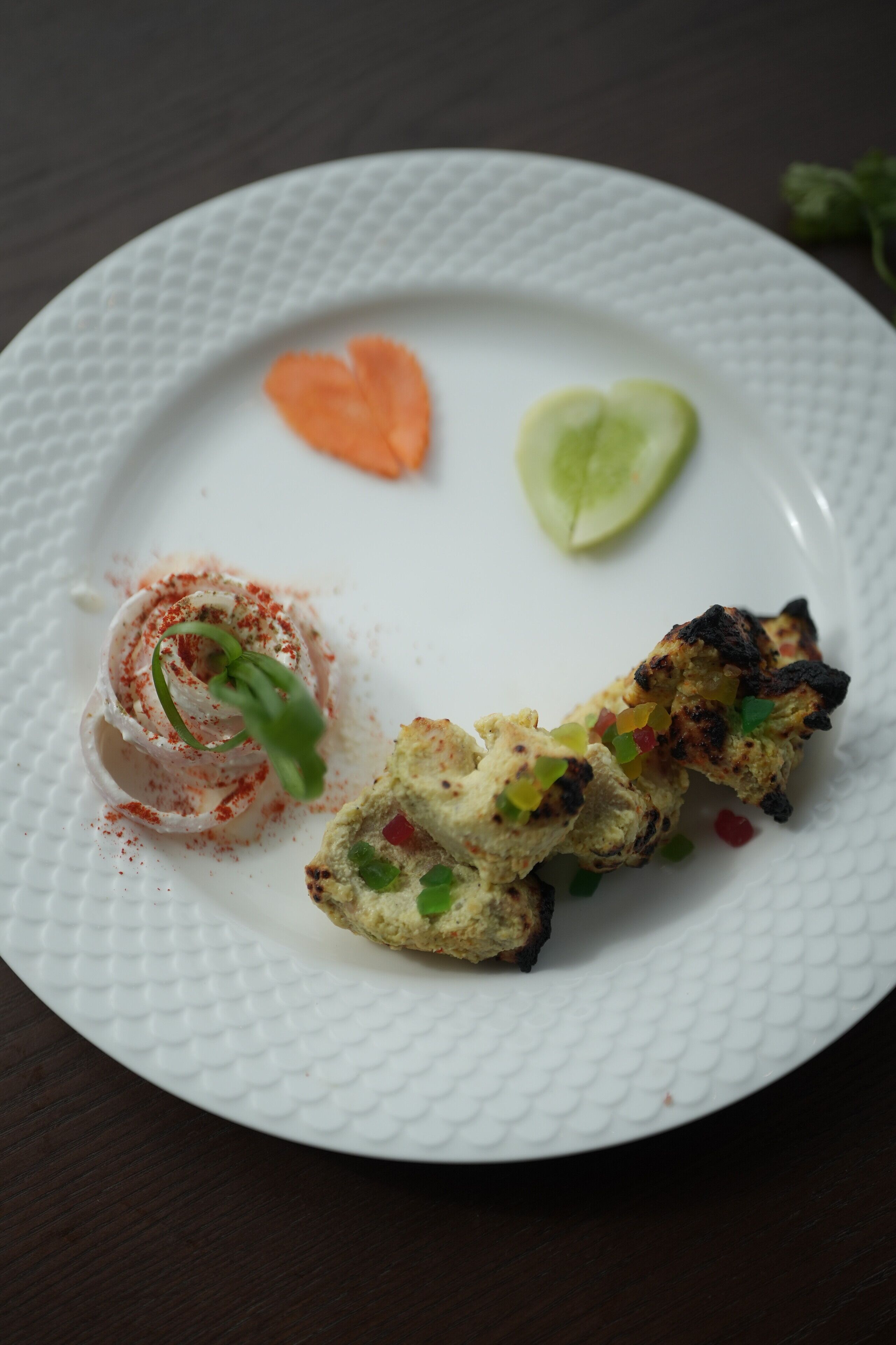 Un piatto bianco con pollo alla griglia, una fetta di lime e un piccolo guarniglio arancione.