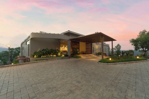 A modern building with a covered entrance, paved driveway, and outdoor seating area. - Ayati Resort & Spa (Kaswand)