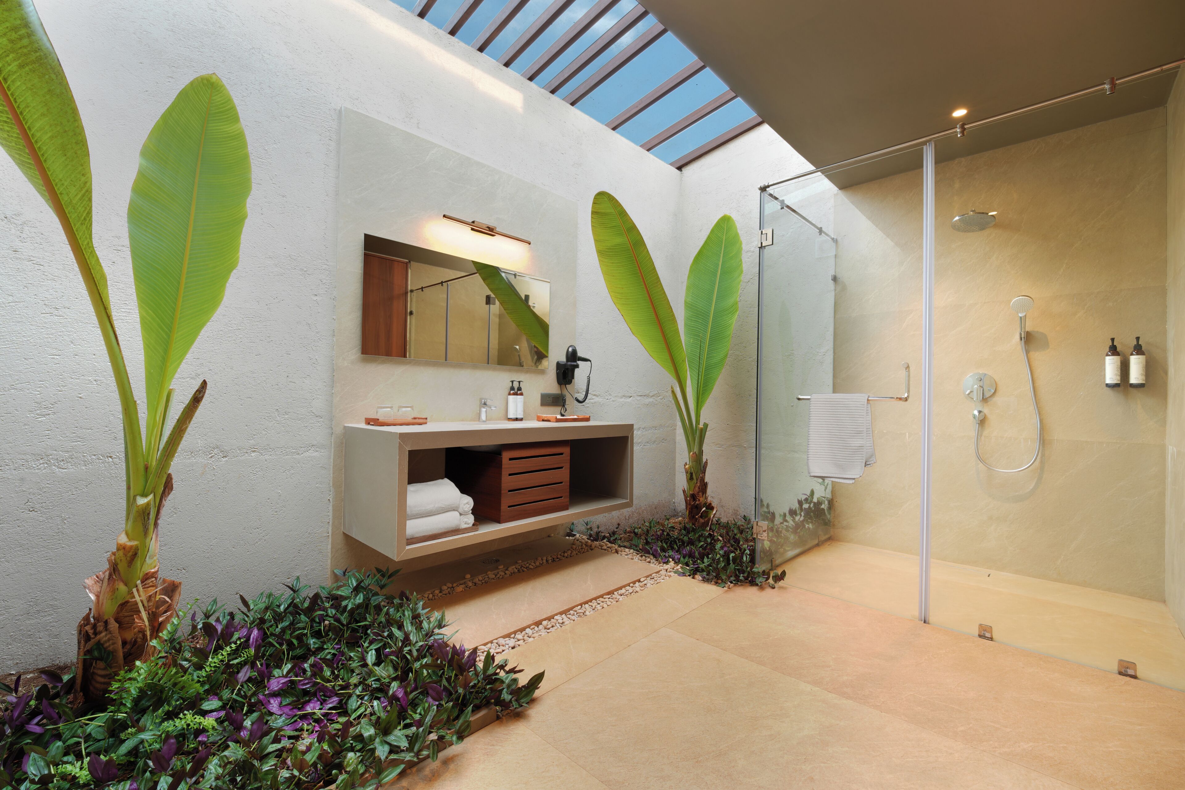 Un baño moderno con tragaluz, ducha con mampara de vidrio y tocador con espejo y toallero.