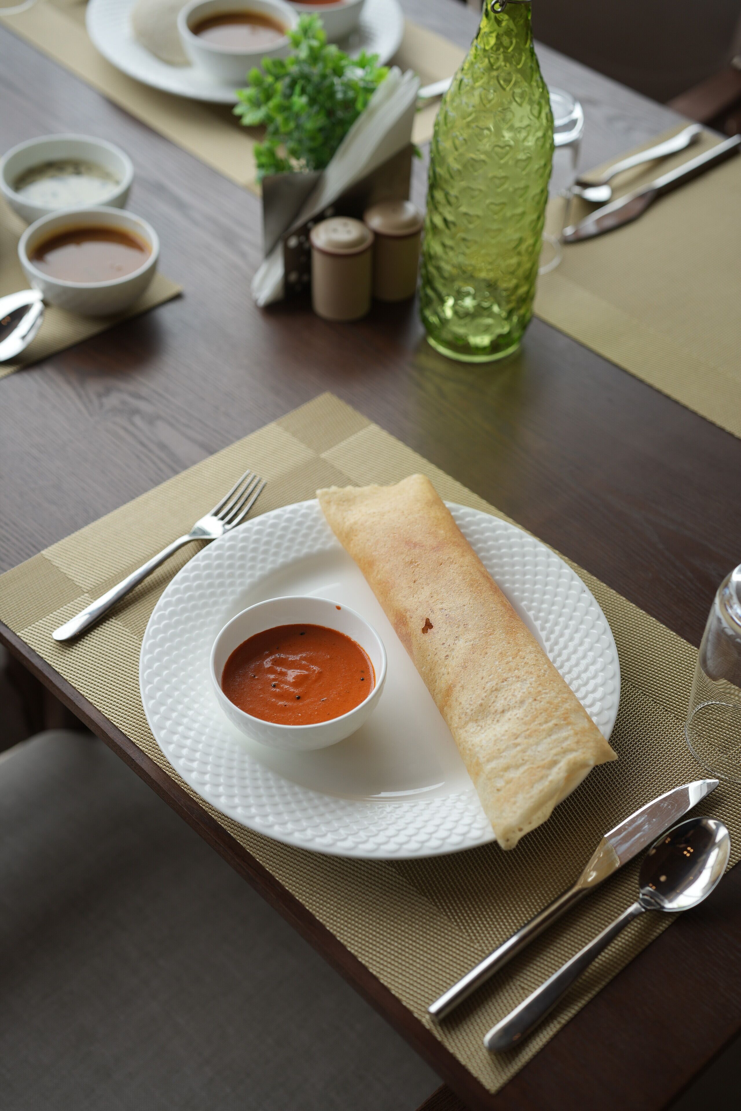 A table set with a plate of food, including a rolled item and a bowl of soup, utensils, and condiments.