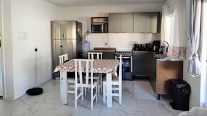 A compact kitchen with a dining table, chairs, a refrigerator, microwave, stove, and a water dispenser.
