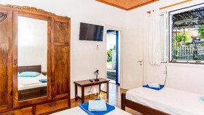 Une pièce avec une armoire en bois, un lit avec un oreiller bleu, une petite table avec une lampe et un téléviseur fixé au mur.