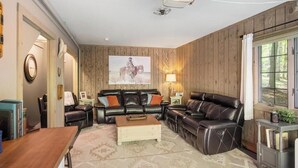 Un salón con una pared de paneles de madera, un sofá de cuero negro, una mesa de centro de madera y un cuadro grande de un caballo.