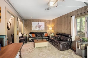 Ein Wohnzimmer mit einer holzverkleideten Wand, einem schwarzen Ledersofa, einem Holztisch und einem großen Gemälde eines Pferdes.