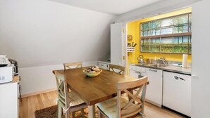 Una cocina compacta con armarios blancos, una mesa de comedor de madera y un ventanal con vistas a árboles.