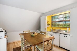 Una cucina compatta con mobili bianchi, un tavolo da pranzo in legno e una finestra vista alberi.